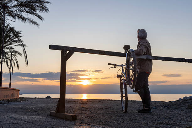 Mature man hangs bicycle on rack by seaside at sunrise, Liguria