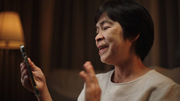 Asian mature woman making video call on sofa at night.