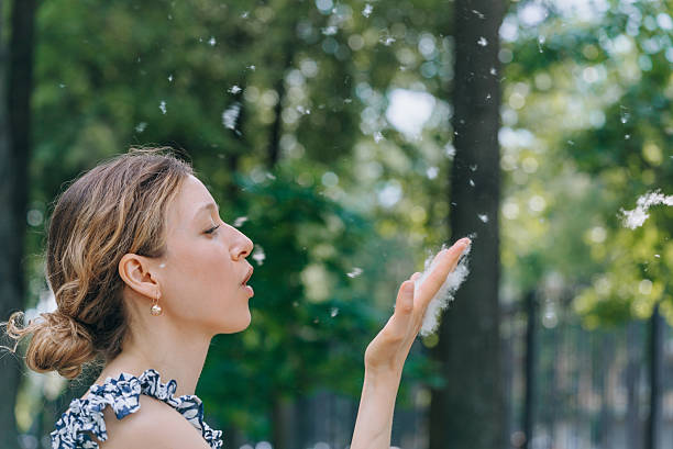 A serene close-up scene showing a hand holding a dandelion releasing seeds into the breeze, set against a natural green background, evoking feelings of serenity, connection with nature, and peaceful moments.