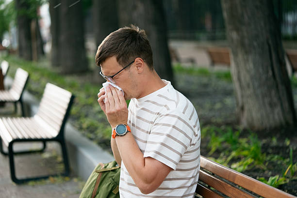 istock Sick man with runny nose or allergy sneezing into tissue while sitting on park bench 2208080437