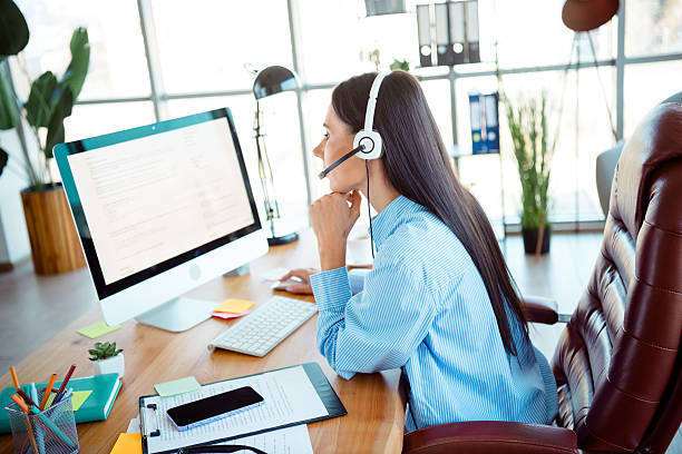 istock Young professional woman working in a modern office environment using a computer and headset 2208081328