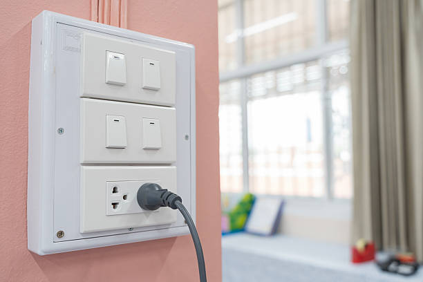 Small white ceramic house model is connected to an electrical outlet with a charging cable, representing the concept of home energy consumption and smart home technology