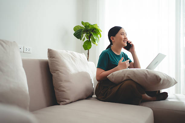 Asian woman enjoyed talking on phone while working on laptop at home. Happy woman working from home.