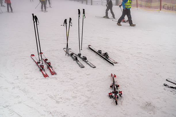 A snowy winter landscape showcasing skis and poles neatly arranged, emphasizing winter sports and recreation. People in the background highlight the active and energetic atmosphere while maintaining a family-friendly environment. Capturing the essence of mountain adventures, this image conveys both leisure and athletic themes.