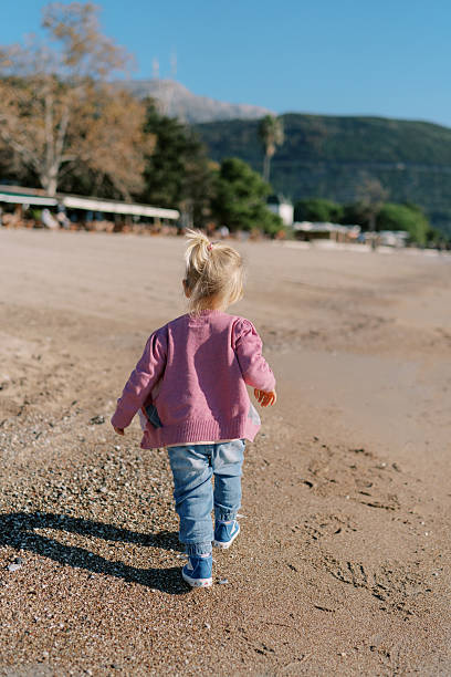 istock Little girl walks along the sandy seashore. Back view 2208086134