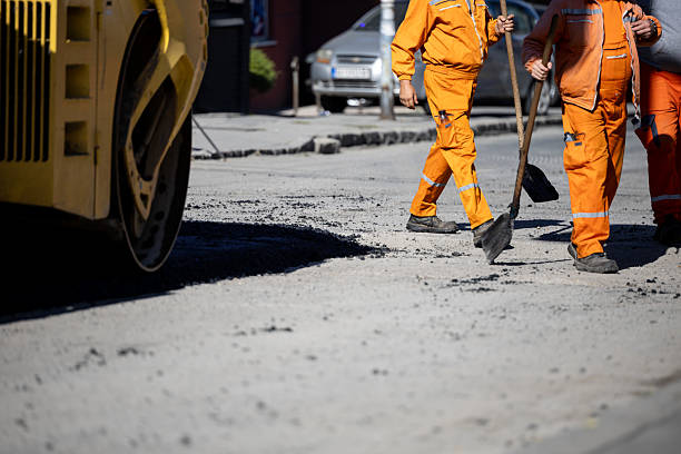 istock Construction workers repair a city street while operating heavy machinery in bright orange uniforms 2208086157