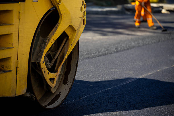 istock Road construction work in progress with a yellow roller and worker smoothing asphalt 2208086321