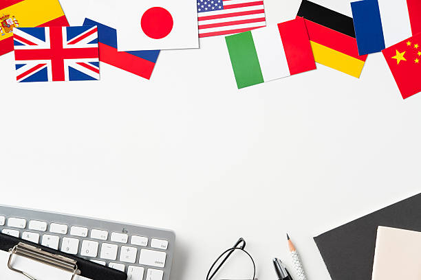 istock Global concept flatlay. Border of international flags (UK, USA, Japan, etc.) above workspace items (keyboard, clipboard, glasses) on white background. Large copy space. 2208087911