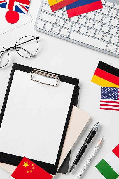 istock International communication concept. Flatlay workspace with keyboard, blank clipboard, glasses, pen, pencil, and world flags on white background. Study or global business theme. 2208087922