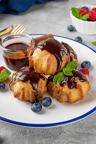 istock Profiteroles with vanilla cream, fresh berries and chocolate glazed on a plate on a gray concrete background. A delicious French dessert. 2208088273