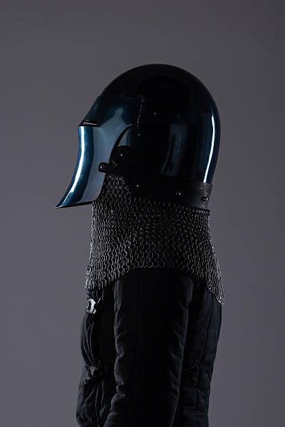 istock Dark Medieval Helmet with Chainmail Collar. This image shows a dark, almost black, medieval helmet with a perforated visor, paired with a silver chainmail collar and a dark garment underneath. 2208088913