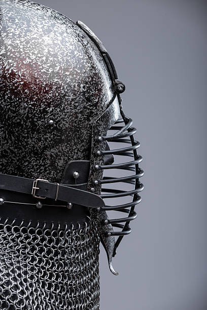 istock Dark Helmet with Ribbed Faceplate and Chainmail. This image shows a dark, possibly blackened steel, helmet with a pointed top and a distinctive faceplate featuring a series of horizontal ribs. A chainmail collar extends from the base of the helmet. 2208089087