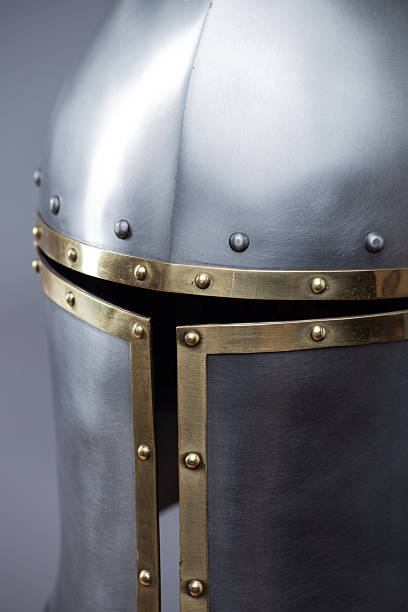 istock Silver Medieval Barbute Helmet with Brass Trim. This image shows a shiny silver helmet with a distinctive T-shaped opening for the face, accented with brass trim and rivets. 2208089154