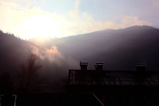 istock Foggy mountains partially obscure houses under a bright, partly cloudy sky 2208089395