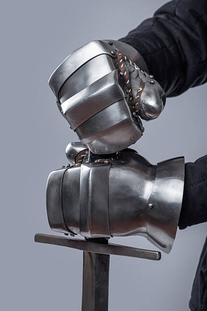 istock Pair of Silver Gauntlets Holding a Sword. This image shows a pair of shiny silver gauntlets, likely made of steel, holding a sword. The gauntlets have articulated fingers and a robust construction. 2208089902