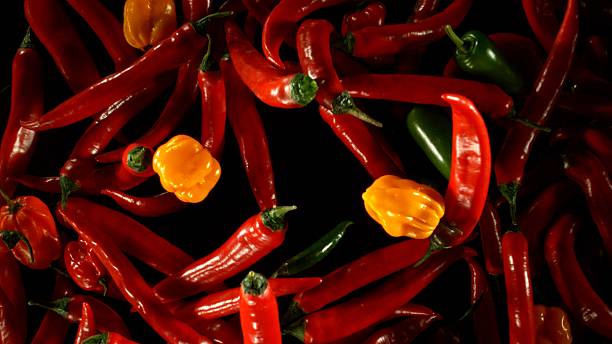 istock Group of coloured chilli peppers flying on black background. 2208090195