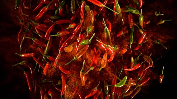 Hot red and green chilli peppers flying on black background. Freeze motion of flying food.
