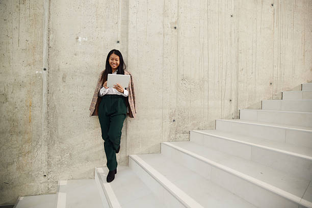 istock Happy Chinese businesswoman using touchpad on staircase in a hallway. 2208093480