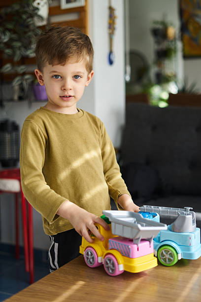 Young boy wearing a red winter coat playing with toy trucks in white sand on a cold, overcast day