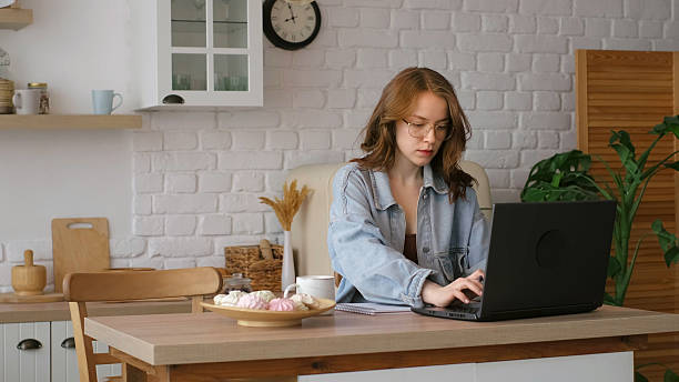 istock Engrossed in her work, a woman writes in a notebook while using a laptop in a bright kitchen. This image reflects the flexibility and comfort of remote work setups in modern homes. 2208101483