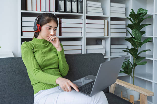 istock Woman sitting comfortably on a couch with headphones, relaxing to music while using a computer in a cozy setting 2208101838