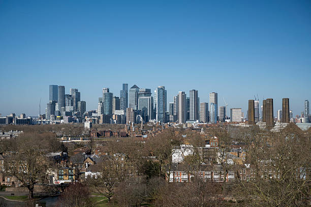 A striking view of Canary Wharf’s modern skyscrapers rising above traditional London homes, showcasing the city’s architectural diversity under a clear blue sky.