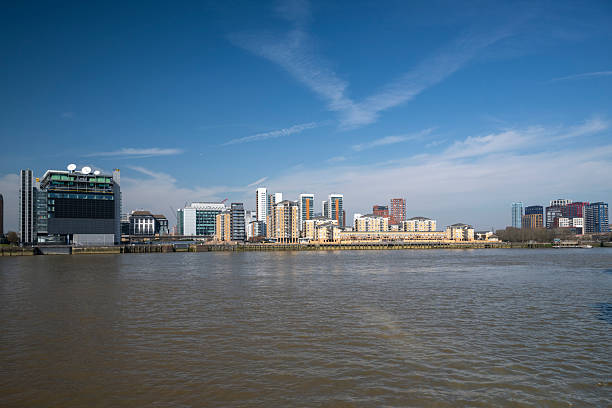A panoramic view of contemporary apartment buildings and office spaces along the River Thames, showcasing the city's evolving skyline under a bright blue sky.