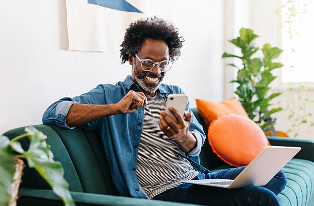 istock Afro mature man smiling and reading a text message on his smartphone at home 2208104723