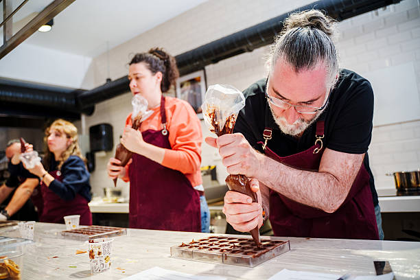 A cook uses a chocolate bag to fill shapes for chocolate desserts during a pastry chocolate making class. Close-up of a dessert master pouring a container for the dessert mass to solidify