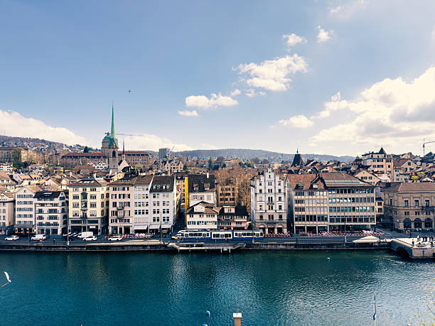 Charming riverside view of a historic European city with colorful buildings and a classic tram passing by. Picturesque urban scene under a bright blue sky. Ideal for travel and tourism.