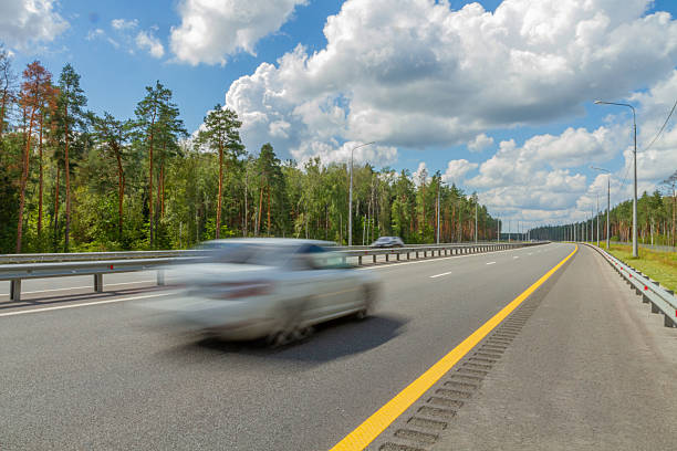 istock A car speeds along a highway through a forest on a sunny day. 2208107533