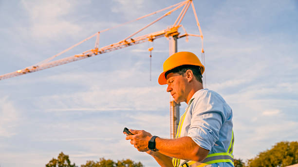 istock Focused Male Construction Worker in Safety Gear Using Smartphone Near Tower Crane 2208108925