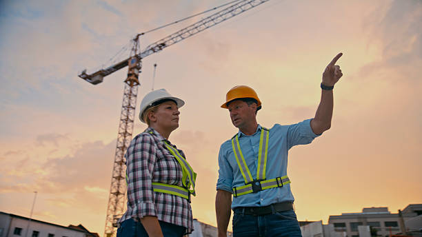 istock Construction Workers Discussing Project at Sunset Wearing Reflective Gear with Tower Crane in Background 2208108958