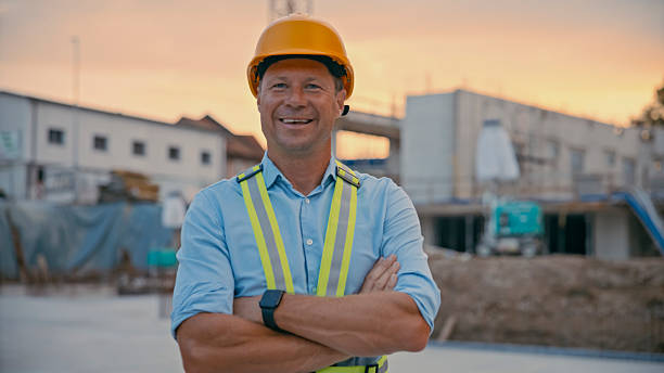 istock Confident Male Engineer Smiling at Construction Site During Sunset with Safety Gear 2208108963