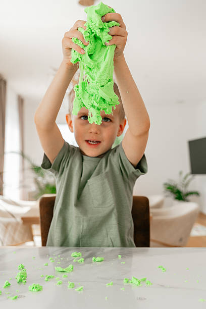 A child enthusiastically pulls apart vibrant green dough, engaging in a hands-on creative play session. The playful moment captures the joy of sensory learning at home.