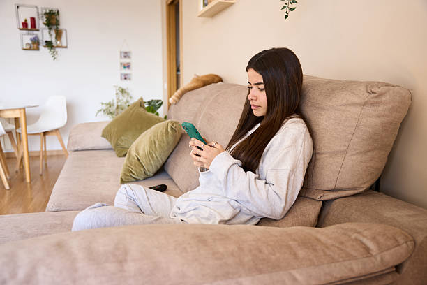 istock Young woman using smartphone while relaxing on sofa at home 2208110317