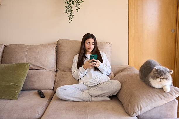 Young woman relaxing on sofa with smartphone and cat