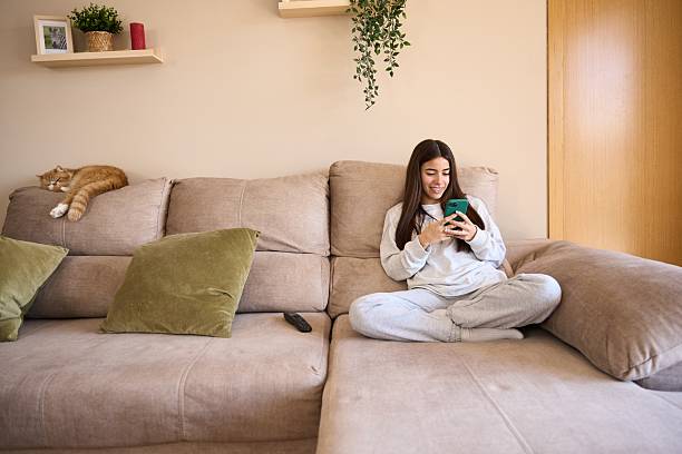istock Young woman relaxing on sofa using smartphone with sleeping cat 2208110336