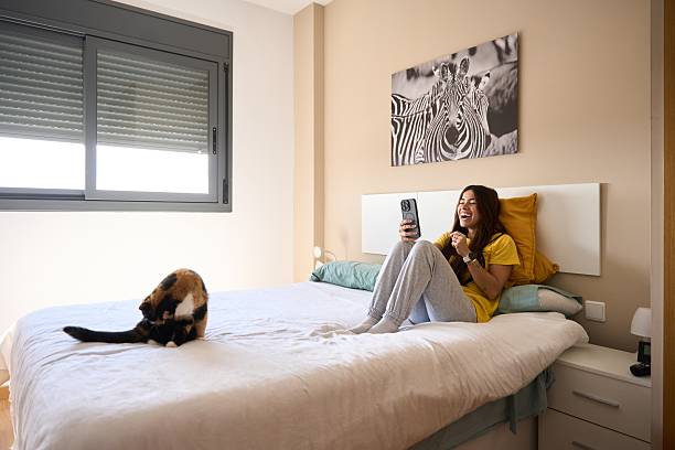 istock Young woman laughing while using smartphone in bed with cat 2208110450