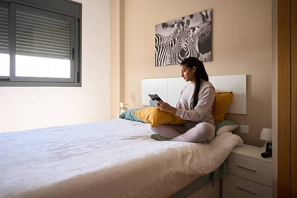 istock Young woman using digital tablet sitting on bed in bedroom 2208110635