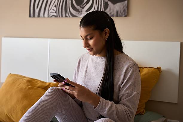 istock Young woman relaxing on bed using smartphone in modern bedroom 2208110660