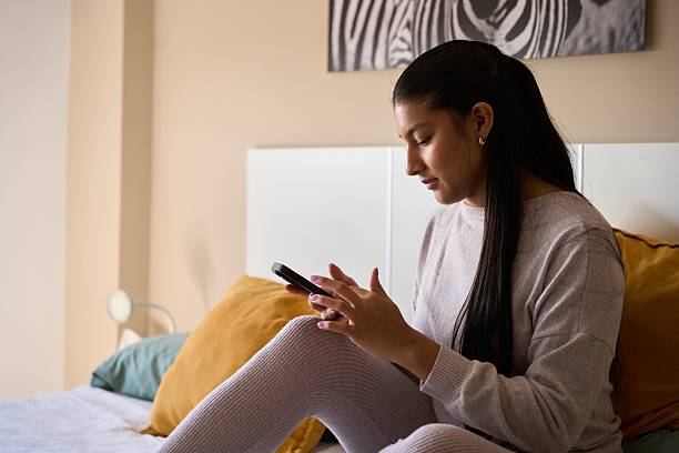 istock Young woman using smartphone on bed in cozy bedroom 2208110667