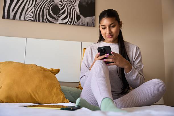 istock Young woman relaxing on bed using smartphone in cozy bedroom 2208110676