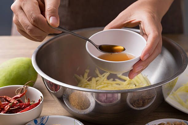 Spicy mango salad cooking, Hand adding fish sauce in bowl and mixing with ingredients