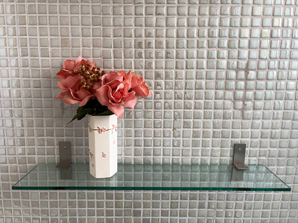 Red color flower on a glass shelf against a grey tile background