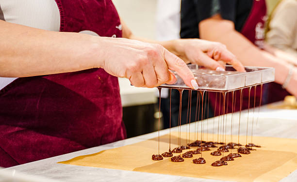 A cook uses a chocolate bag to fill shapes for chocolate desserts during a pastry chocolate making class. Close-up of a dessert master pouring a container for the dessert mass to solidify and he turns over the candy mold and the excess chocolate is poured