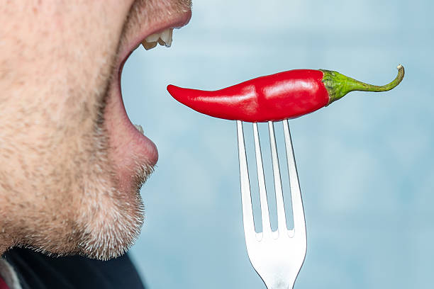 istock red pepper on a fork while eating. Portrait of young man eating chili pepper 2208126630