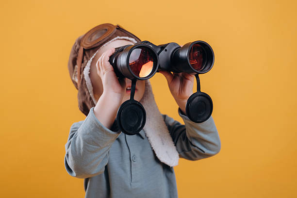 istock Black binoculars in hands, in aviator hat. Cute little boy is against yellow background 2208130581