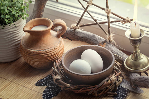 Home spring altar. Bowl with eggs, clay jug with milk, candle, pentacle and birds feathers under the sun's rays.