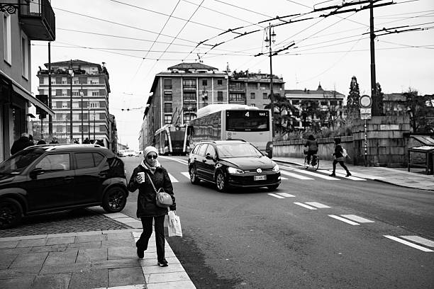 Parma, Italy, March 1, 2025: Urban landscape with pedestrians on the sidewalk, cyclist, and orange city bus in motion.